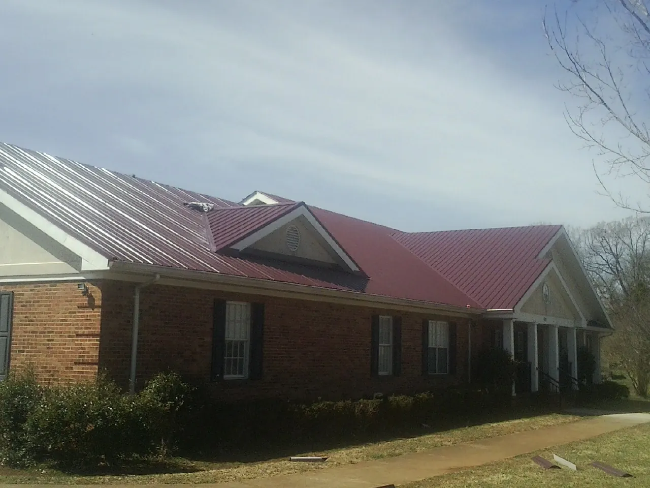 Red metal roof with gabled entries on a long brick building, from a Hail Damage Roof Repair job in Stanton