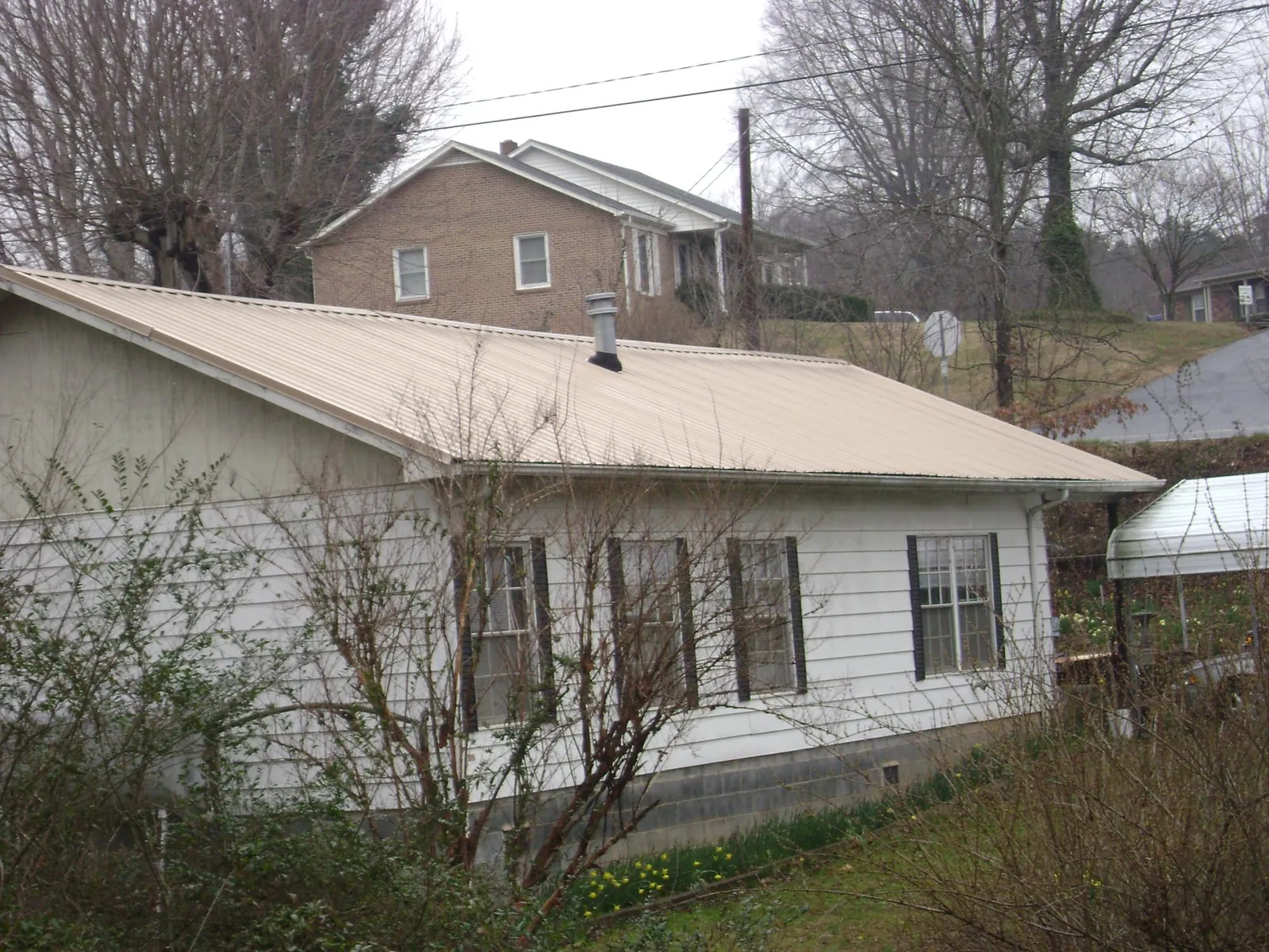 Tan metal roof on a white sided house set into a hillside — Commercial Roofing by Roofing Brothers in Stanton